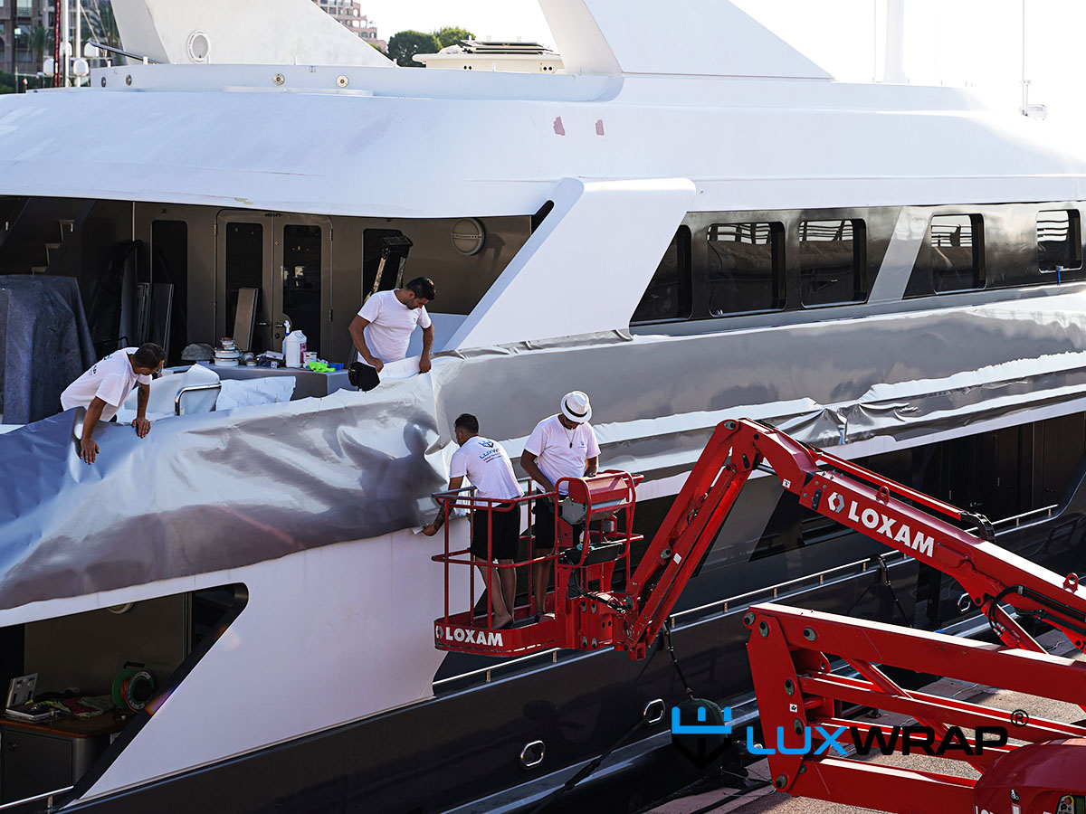 LuxWrap installers applying superyacht exterior wrap using access platforms during a large-scale yacht wrapping project