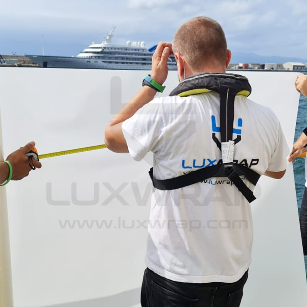 LuxWrap installer measuring and trimming paint protection film on the hull of a 110m Feadship