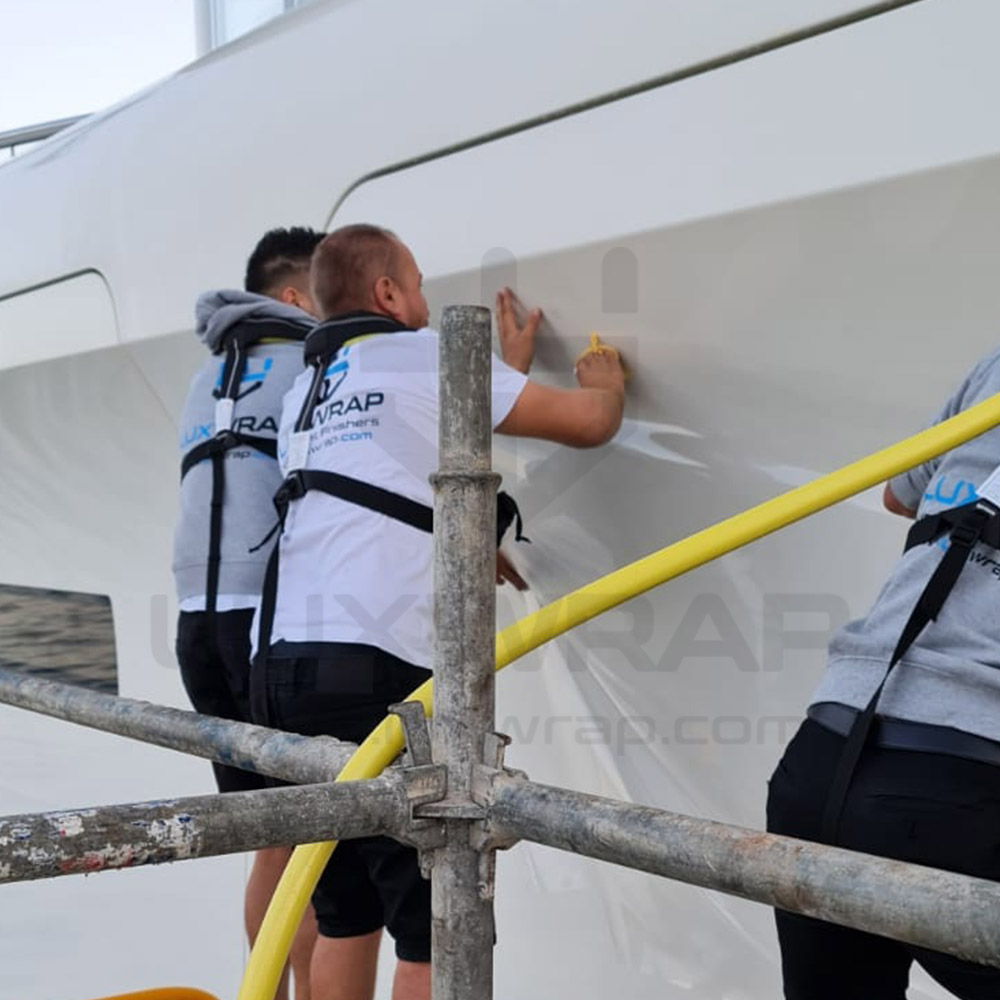 LuxWrap specialist pressing and smoothing PPF onto a 110m Feadship hull section from scaffolding