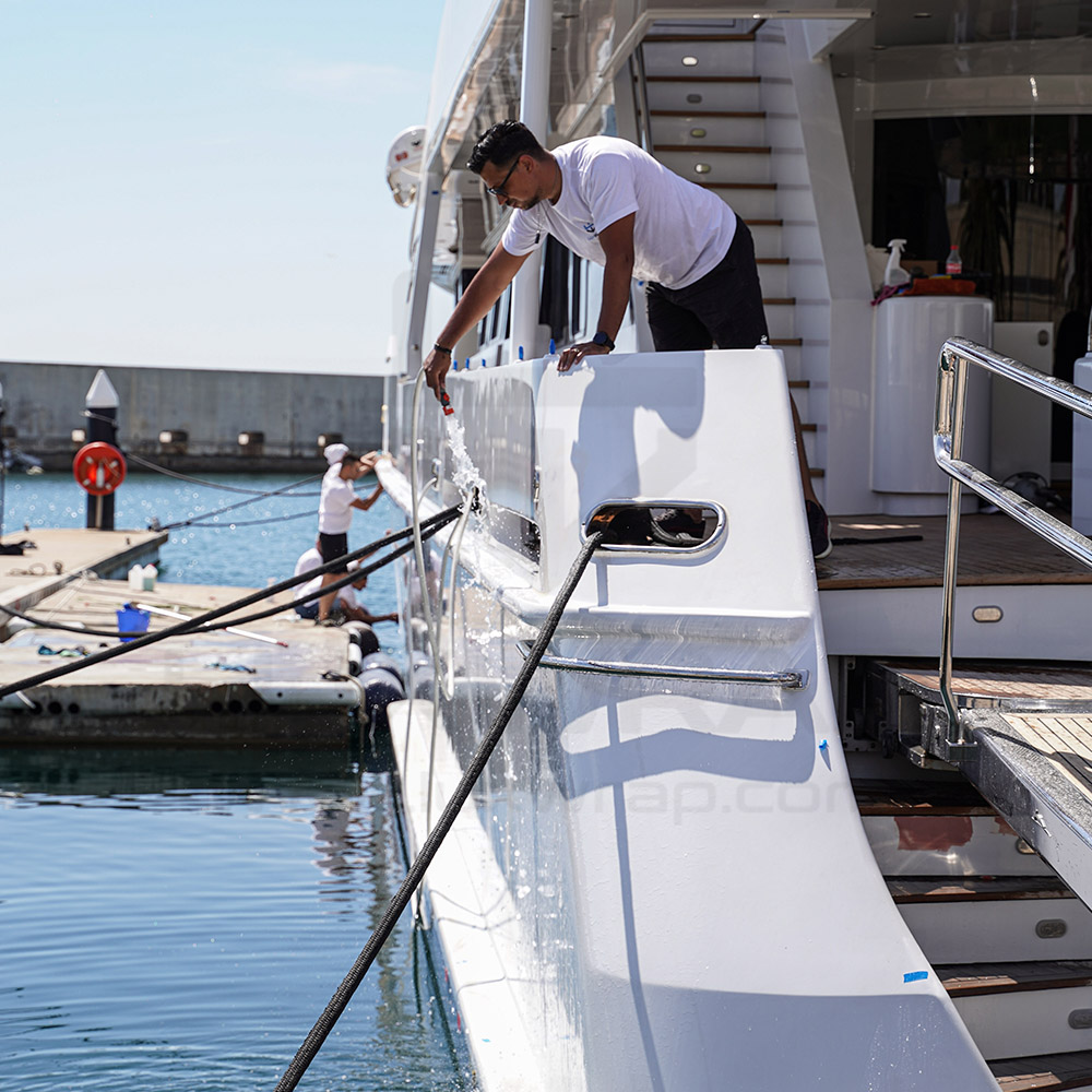 LuxWrap installer applying metallic white vinyl to the hull of a 43m Heesen superyacht from a floating raft
