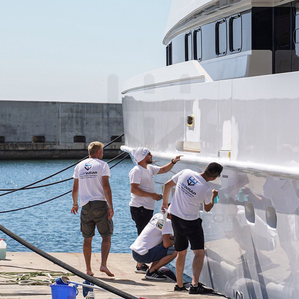 Metallic white vinyl wrap being fitted to the hull of a 43m Heesen — LuxWrap in-water installation with no yard infrastructure