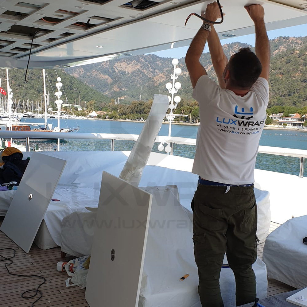 LuxWrap installer trimming and fitting satin-white vinyl around deckhead fixtures on a 57m Benetti